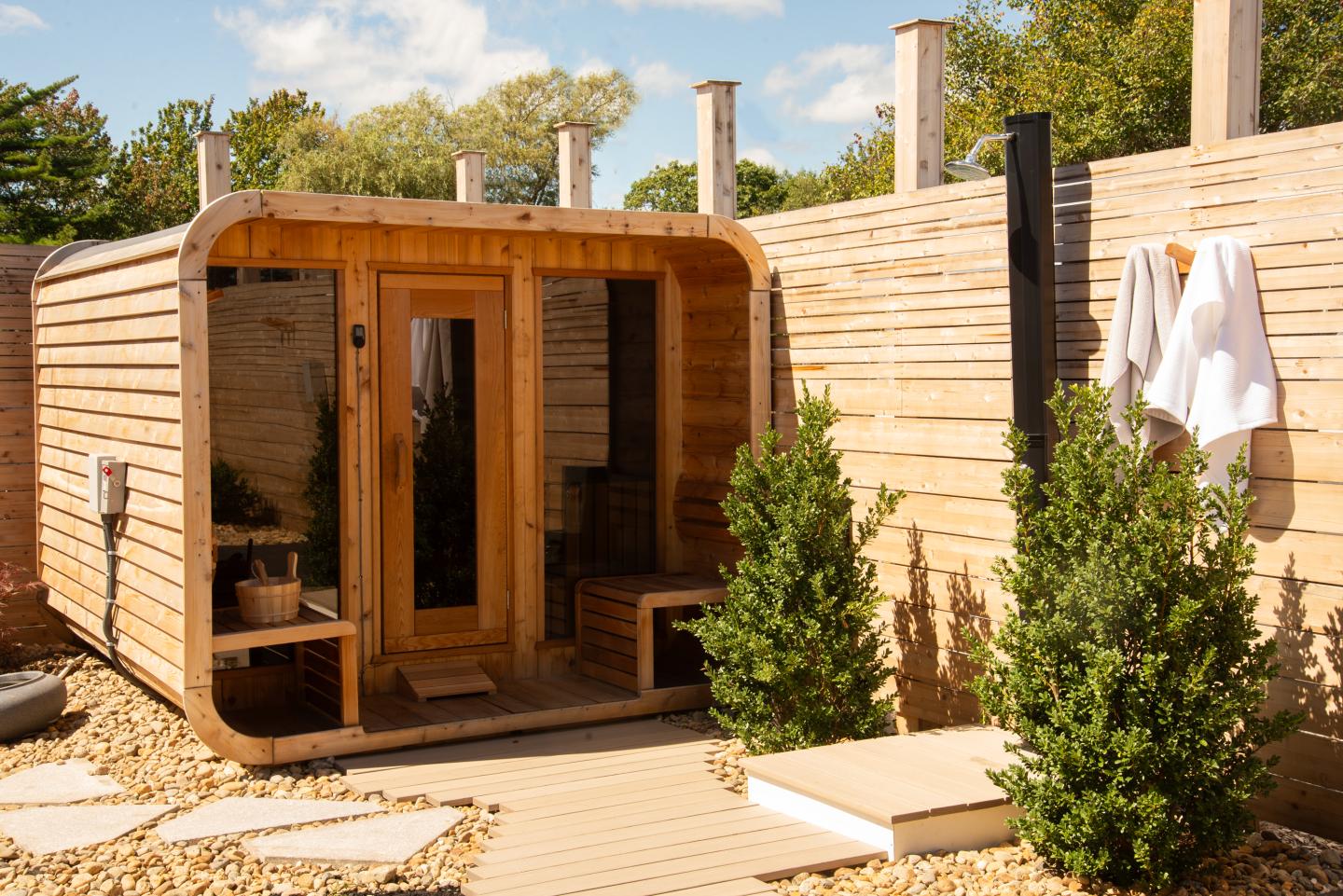 Wooden outdoor sauna surrounded by small green bushes.