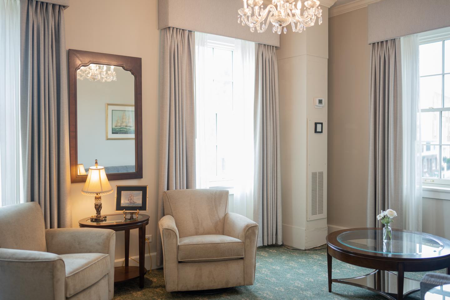 Elegant sitting area with armchairs, chandelier, and large windows.