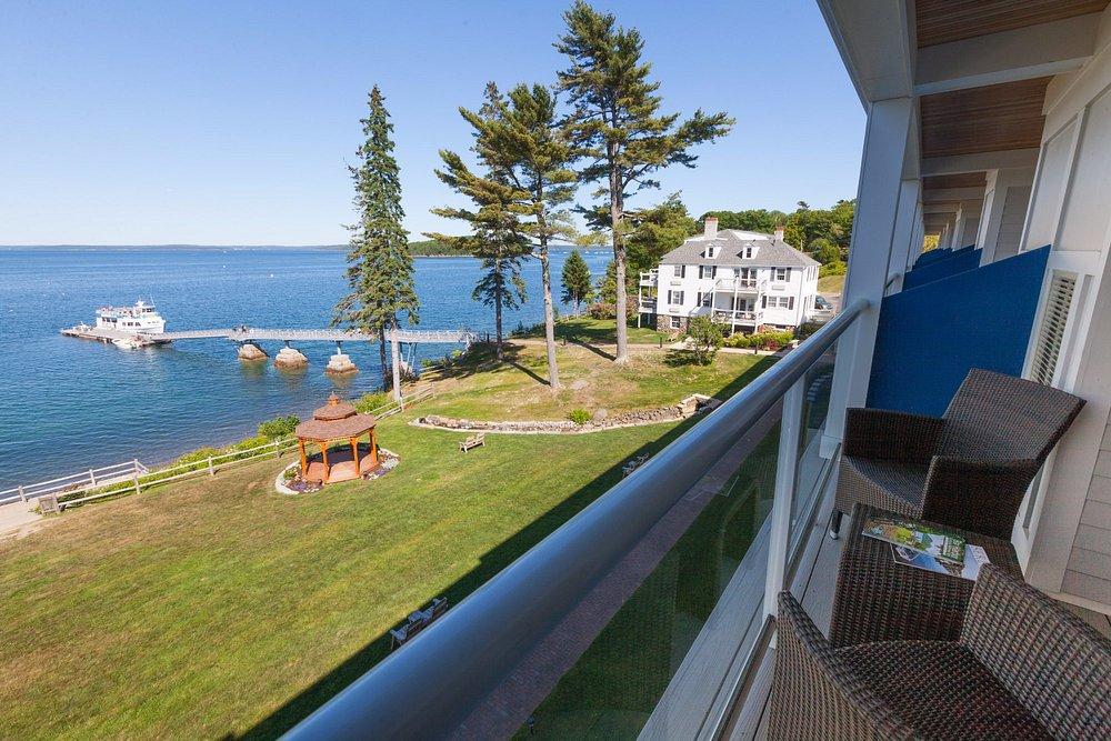 Balcony with chairs, overlooking a lakeside lawn, pier, and house.