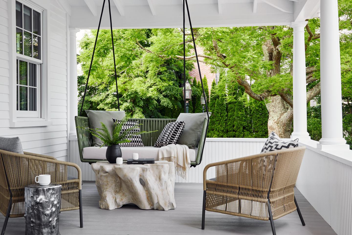 Porch with a hanging swing sofa, wicker chairs, and a green garden view.
