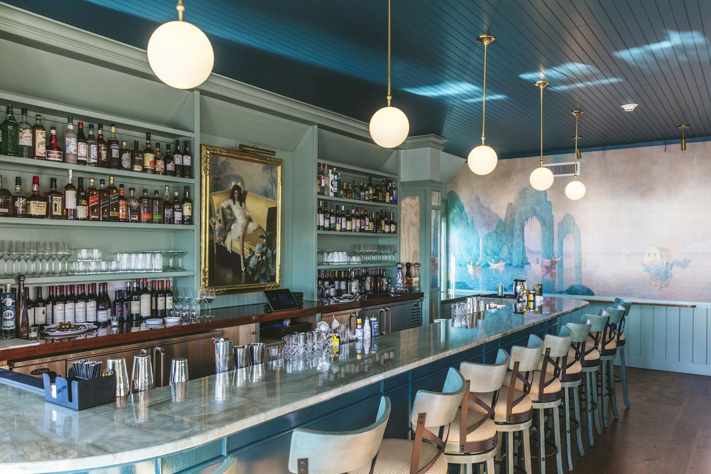 Stylish bar with teal decor, globe lights, and wall mural.