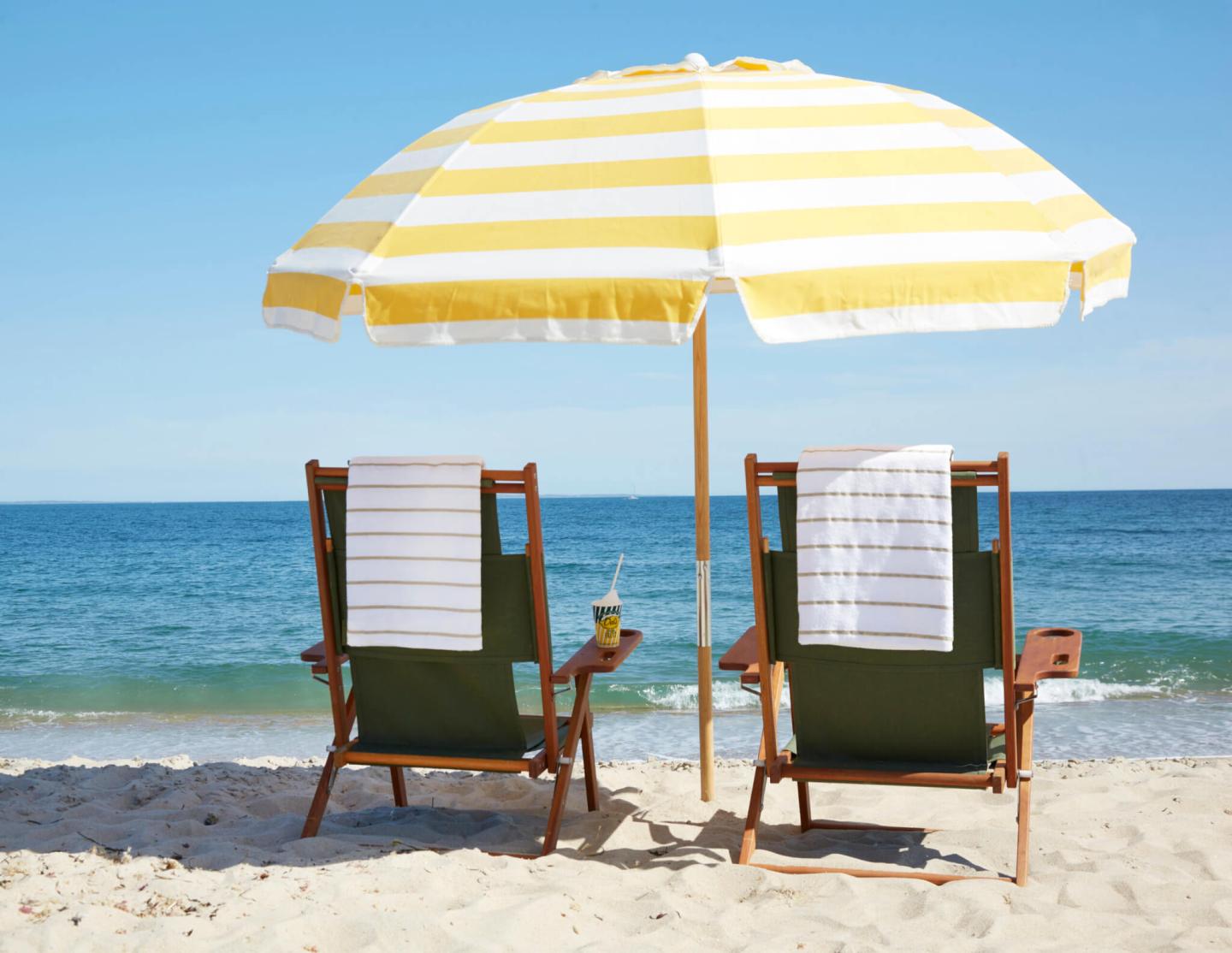 Two deck chairs under a yellow-striped umbrella on a sandy beach.