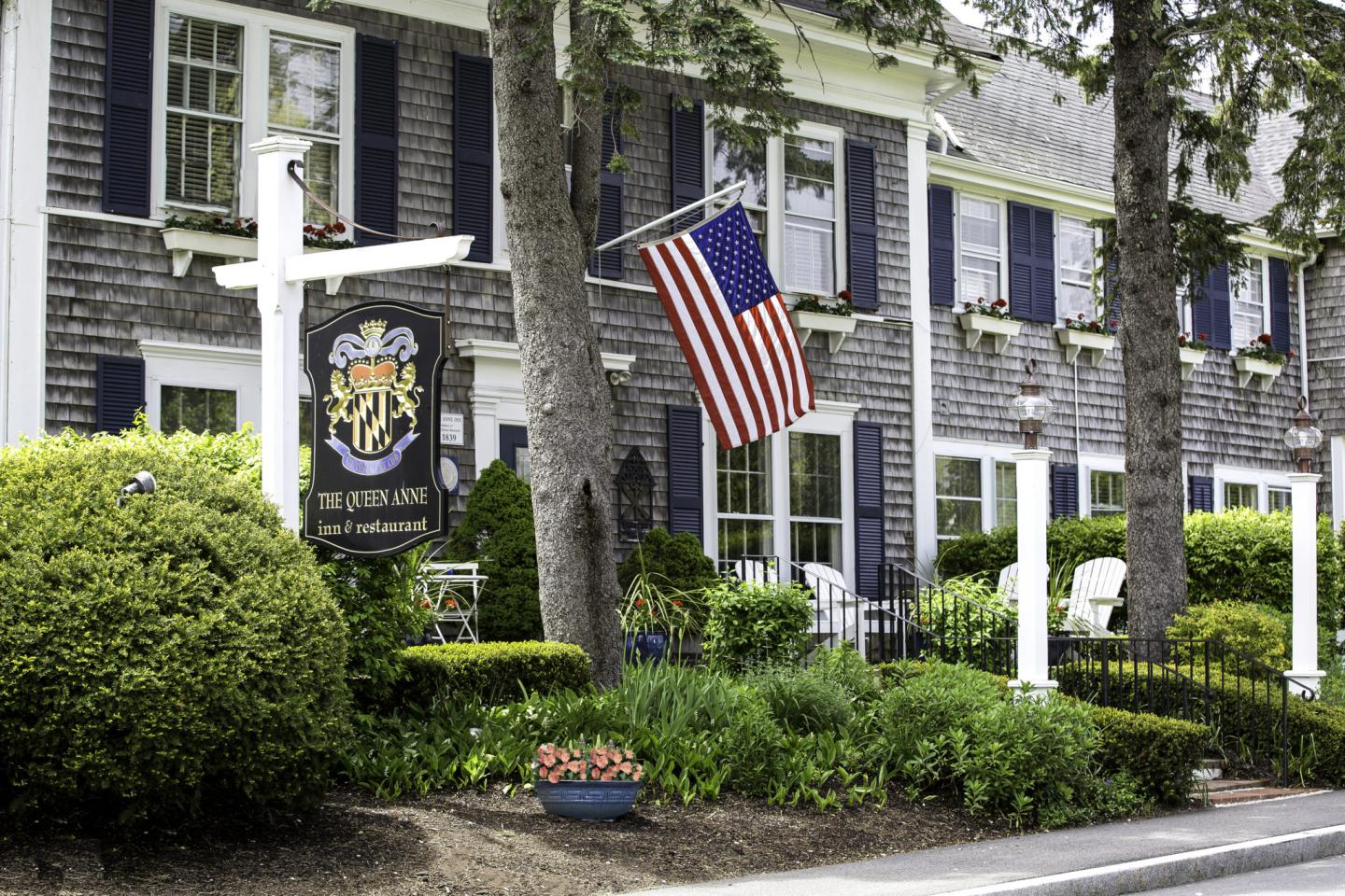 Historic inn with American flag and flower garden in front.