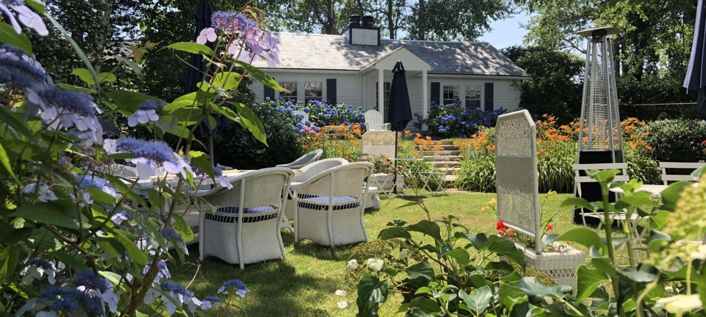 Sunny garden patio with white chairs and vibrant flowers.