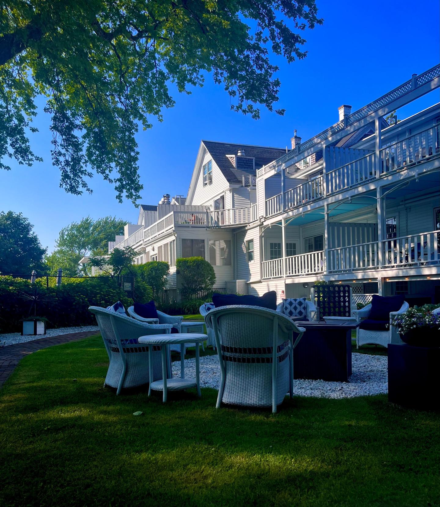 White wicker chairs on a lawn by a large white house under a clear blue sky.ro 03.