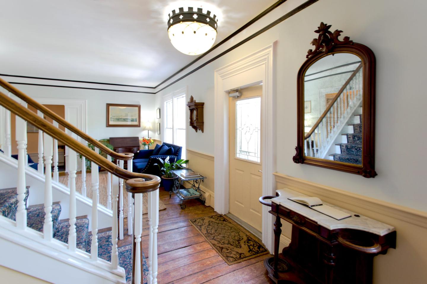 Elegant foyer with wooden staircase, ornate mirror, and chandelier.
