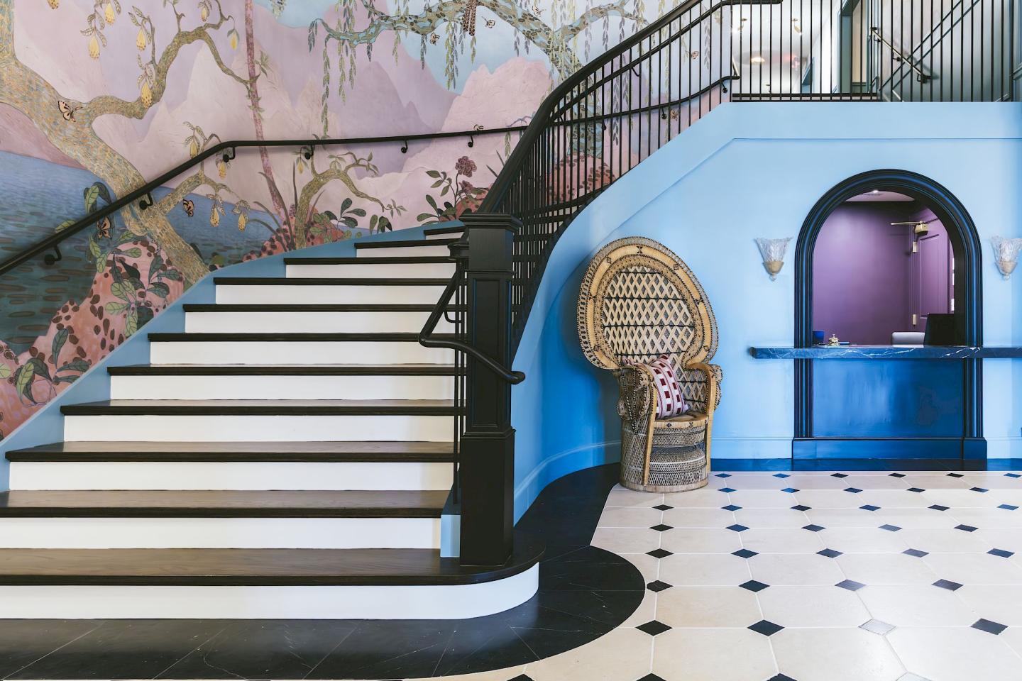 Staircase with floral wall mural, blue reception desk, and wicker chair.