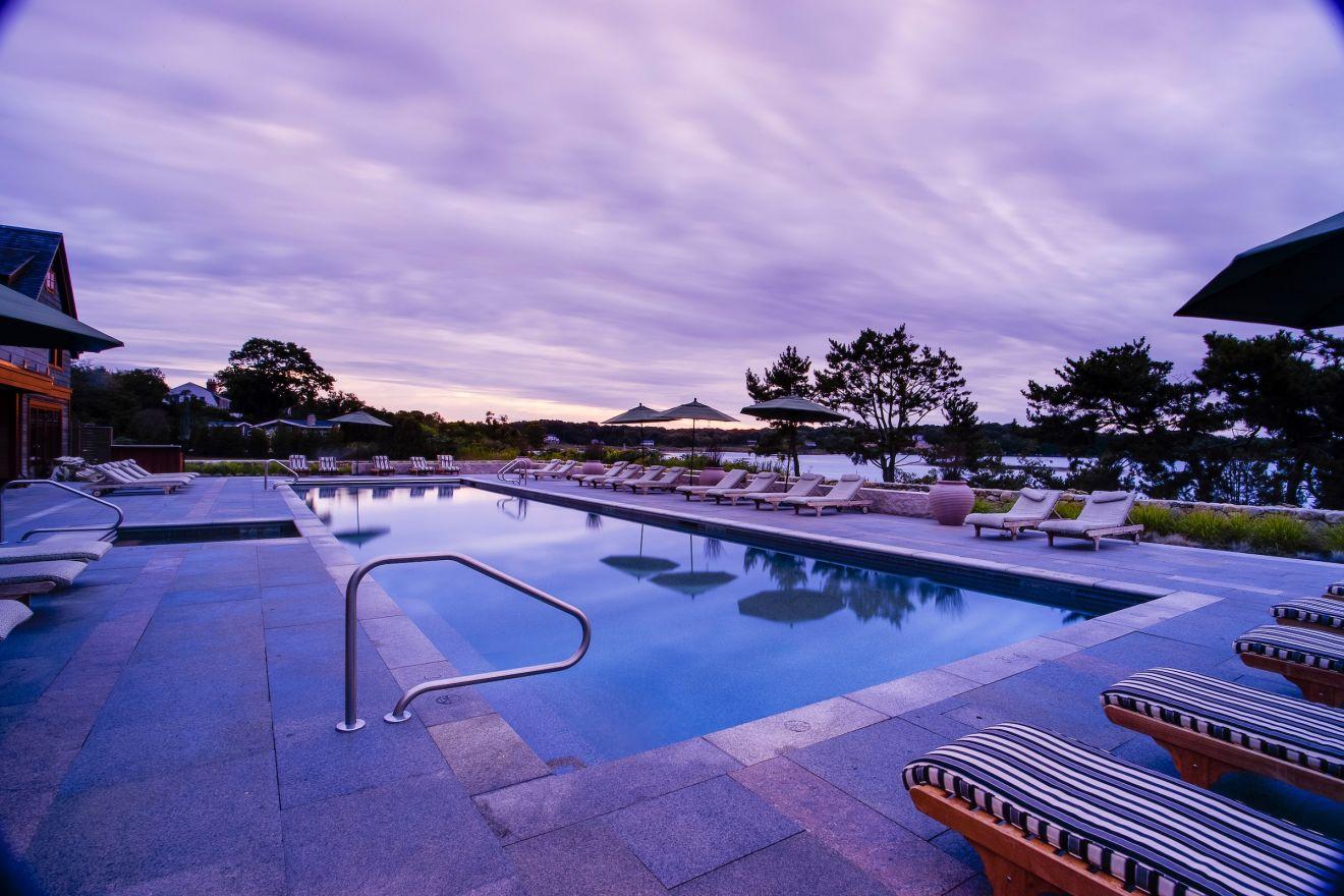 Outdoor pool at sunset with lounge chairs and purple sky.