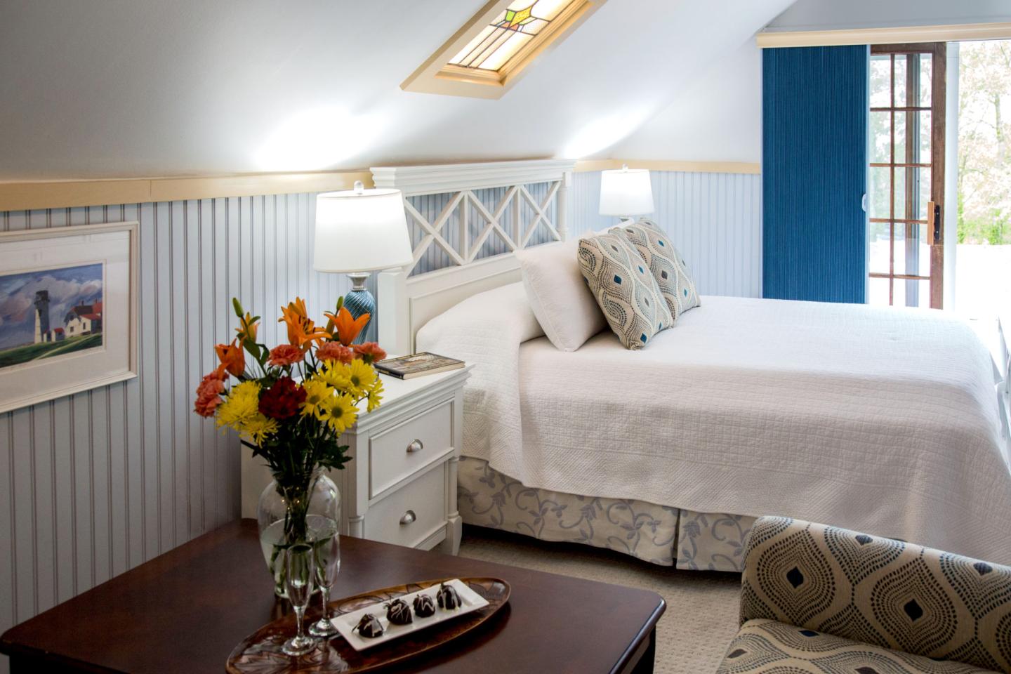 Cozy bedroom with skylight, white bed linens, and colorful flowers on a bedside table.