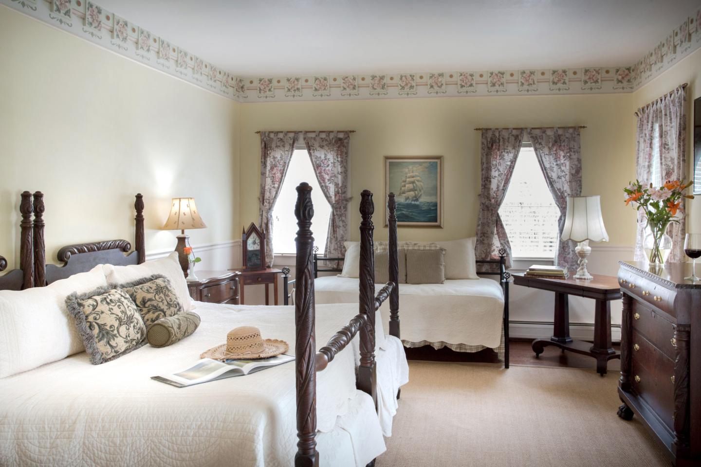 Elegant bedroom with twin beds, floral curtains, and a serene painting on yellow walls.