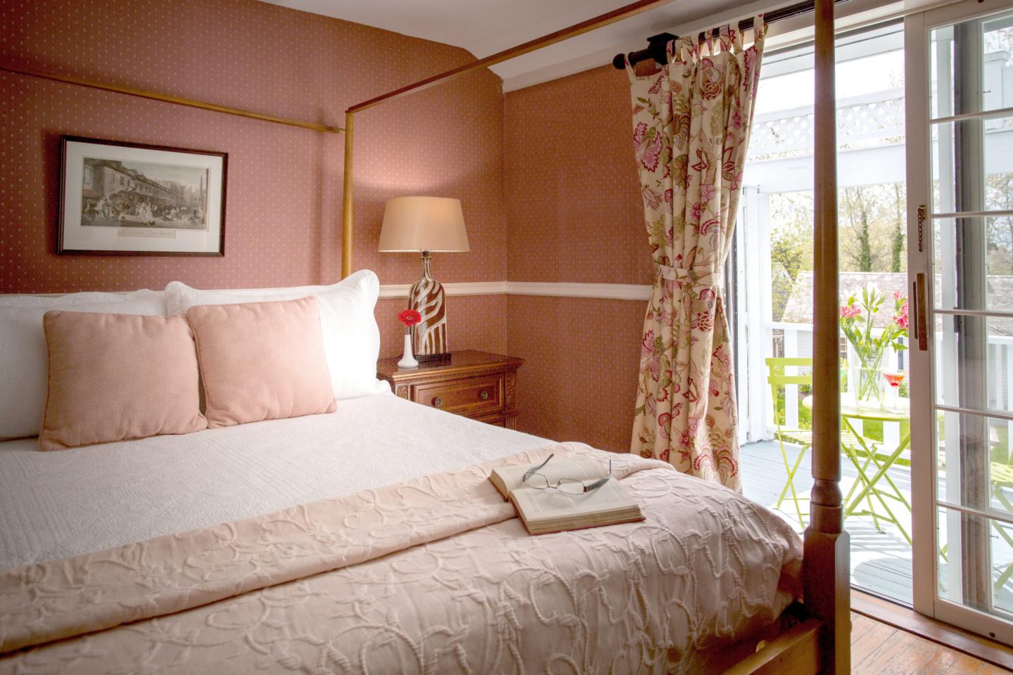 Cozy bedroom with a bed, pink walls, and open patio doors to a garden.