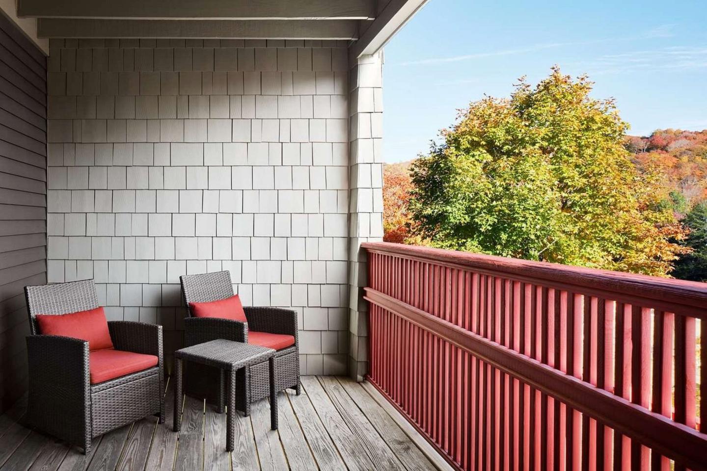 Balcony with two chairs, small table, and view of trees in autumn.