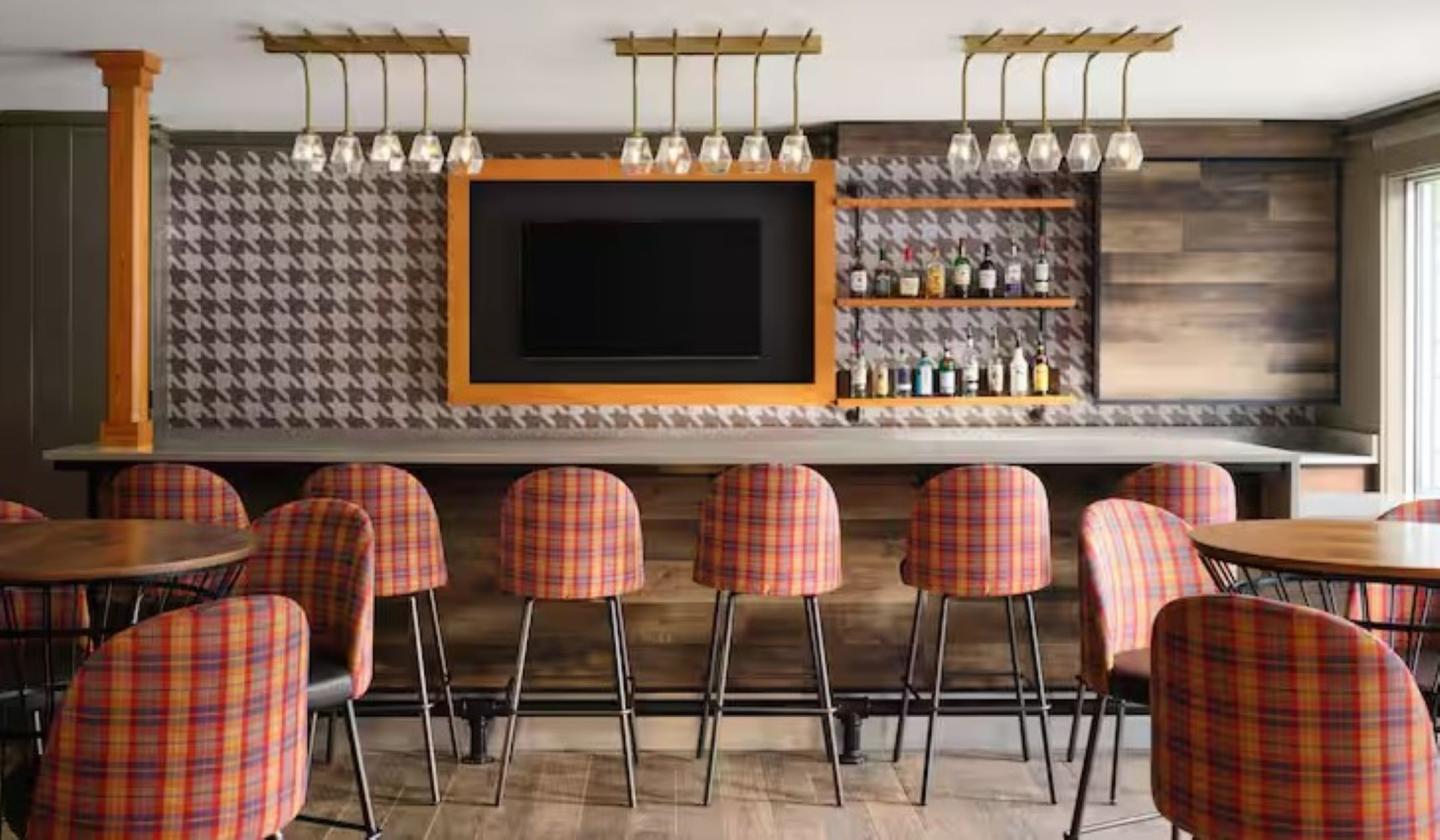 Bar with plaid chairs, a widescreen TV, and shelves of bottles on a patterned wall.r