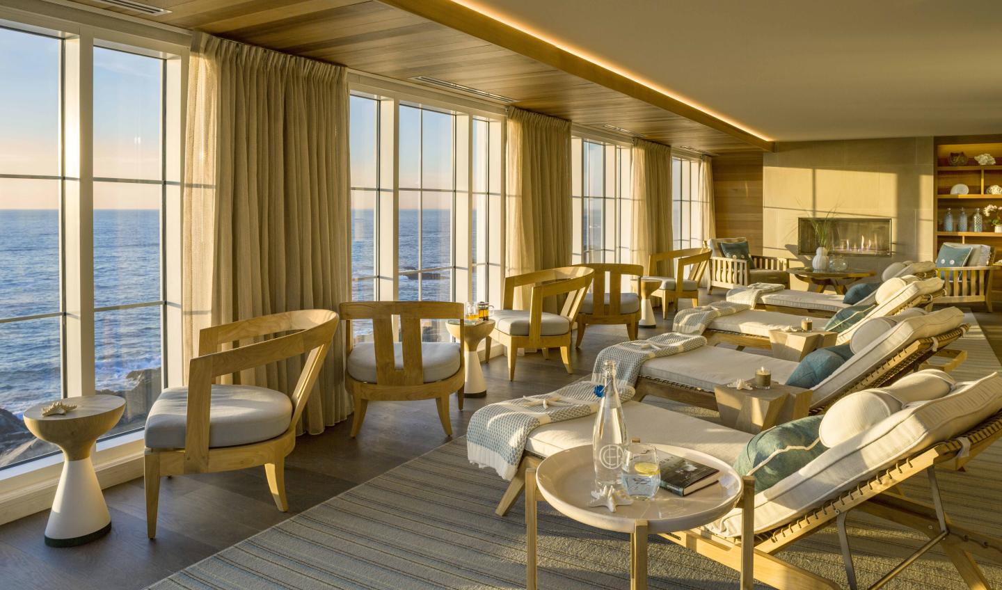 Relaxing lounge with wooden furniture, ocean view through large windows.