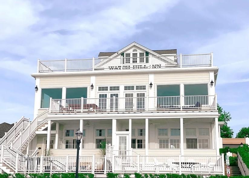 Elegant white coastal house with large windows and balconies under a blue sky.