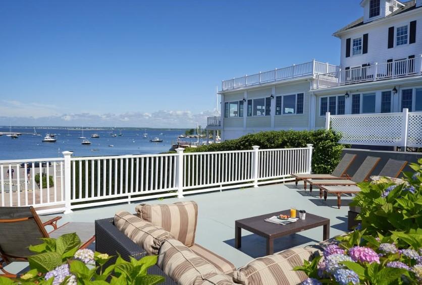 Rooftop patio with striped couches, overlooking a calm sea and boats.