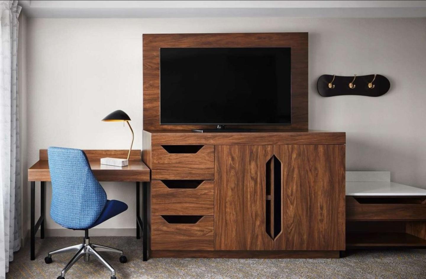 Hotel room with a blue chair, desk, and large wooden TV cabinet.