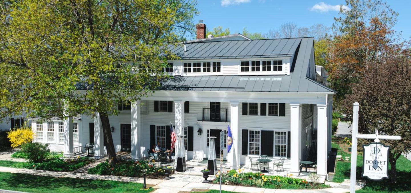 White colonial house with columns, flags, and a metal roof, surrounded by trees.o