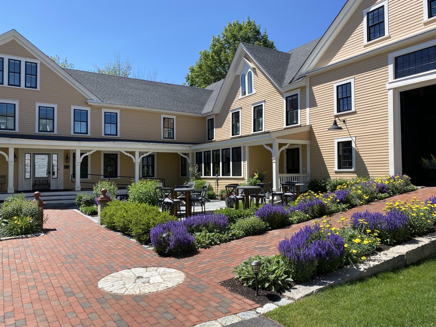 Historic beige house with a brick courtyard and vibrant flower garden.