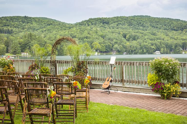 Outdoor wedding setup by a lake with chairs, floral arch, and guitar.