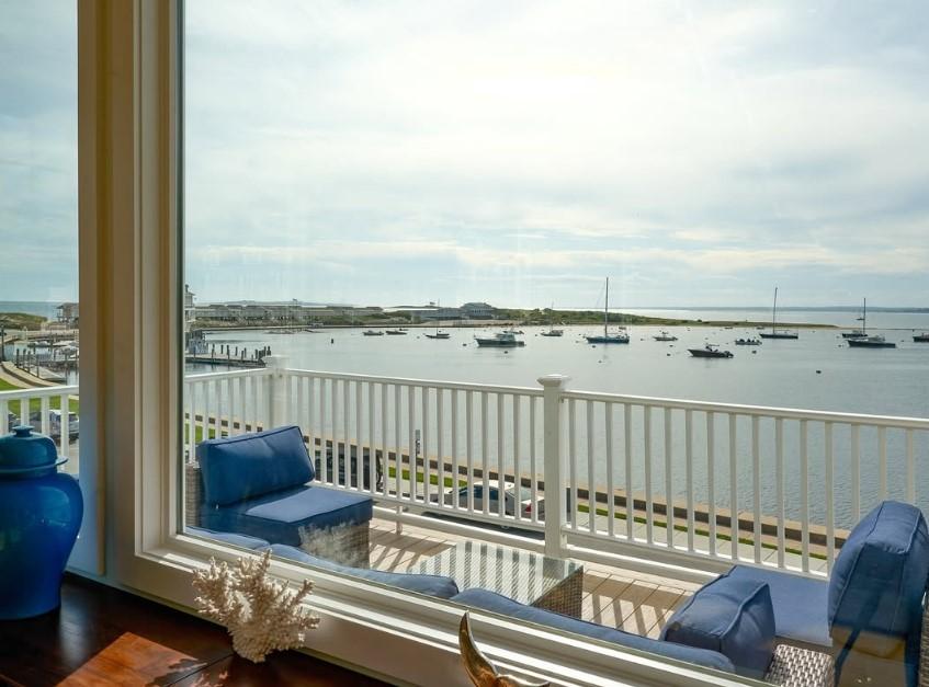 View of a harbor with boats through a window, blue cushions on balcony chairs.