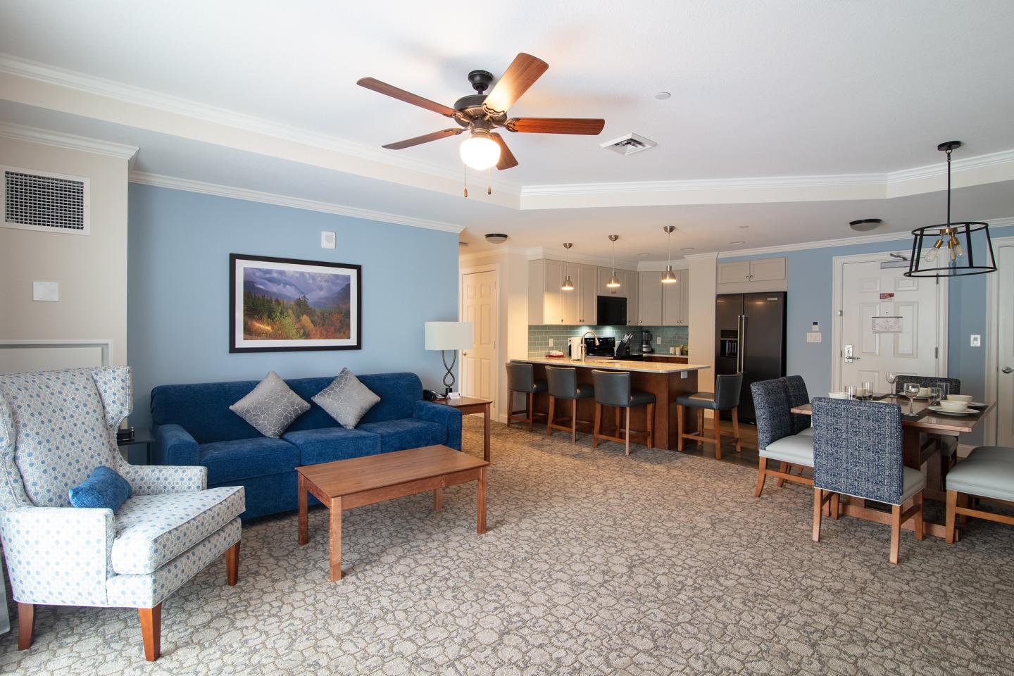 Spacious living room and kitchen with blue sofa, ceiling fan, and dining area.