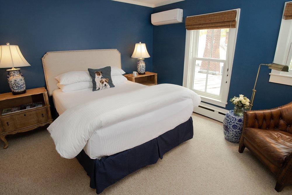 Cozy bedroom with blue walls, white bedding, and brown leather chair.