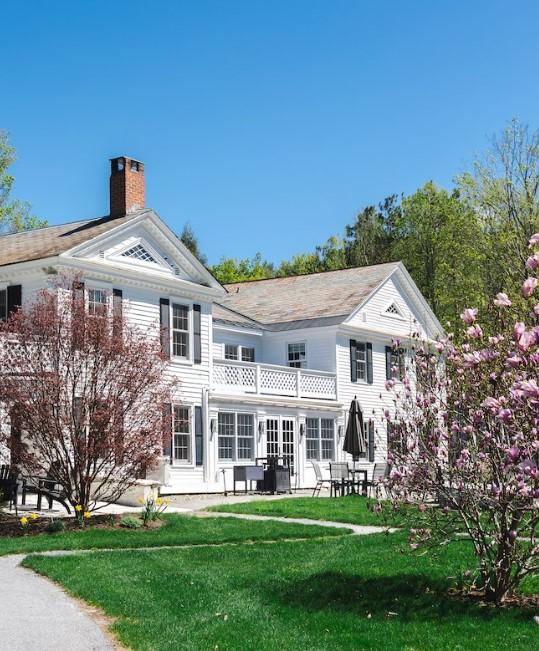 White house with trees and green lawn under blue sky.