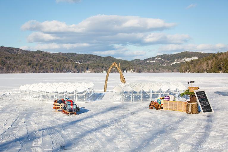 Winter outdoor wedding setup on a frozen lake with white chairs and arch.