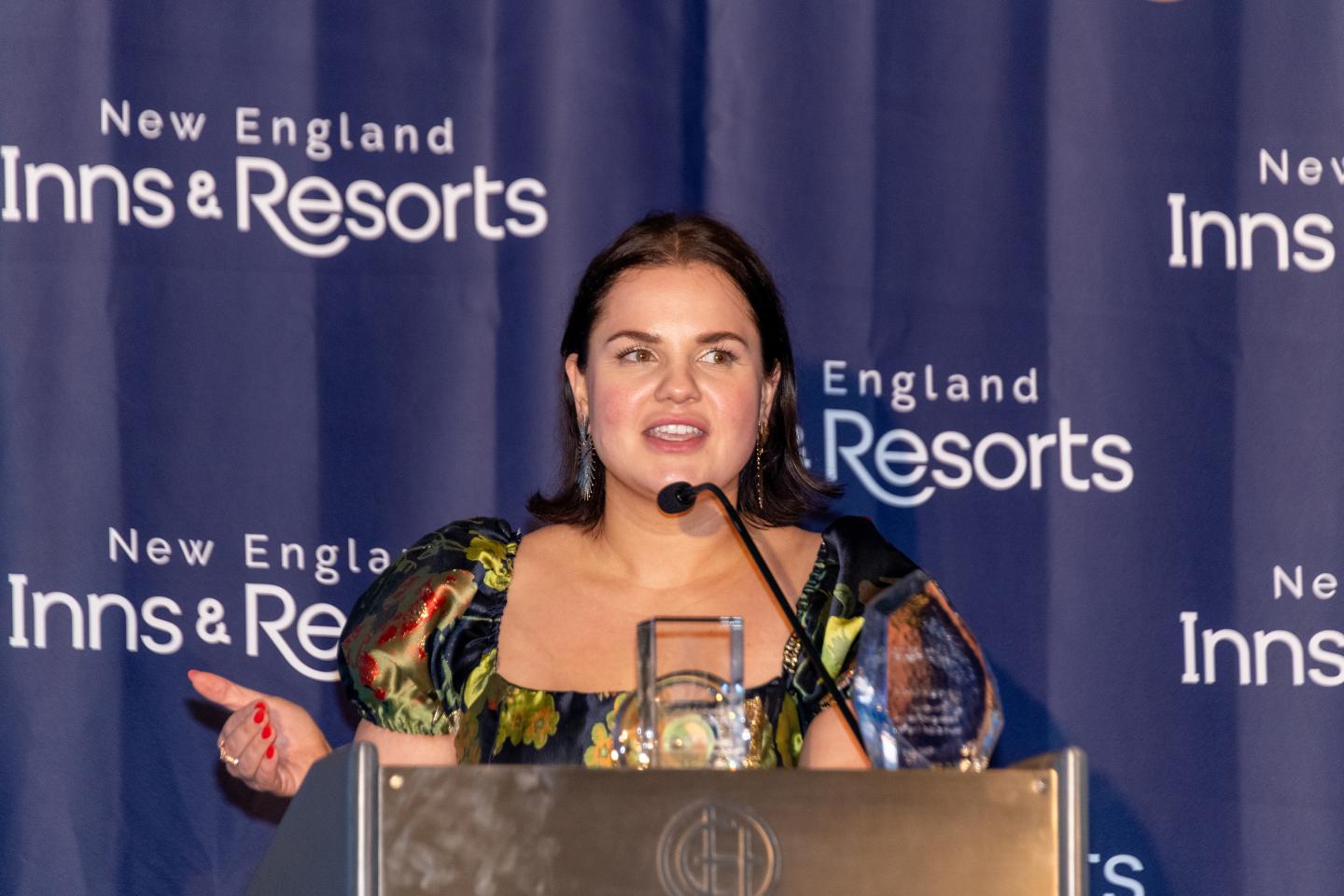 Woman speaking at a podium with a "New England Inns & Resorts" backdrop.