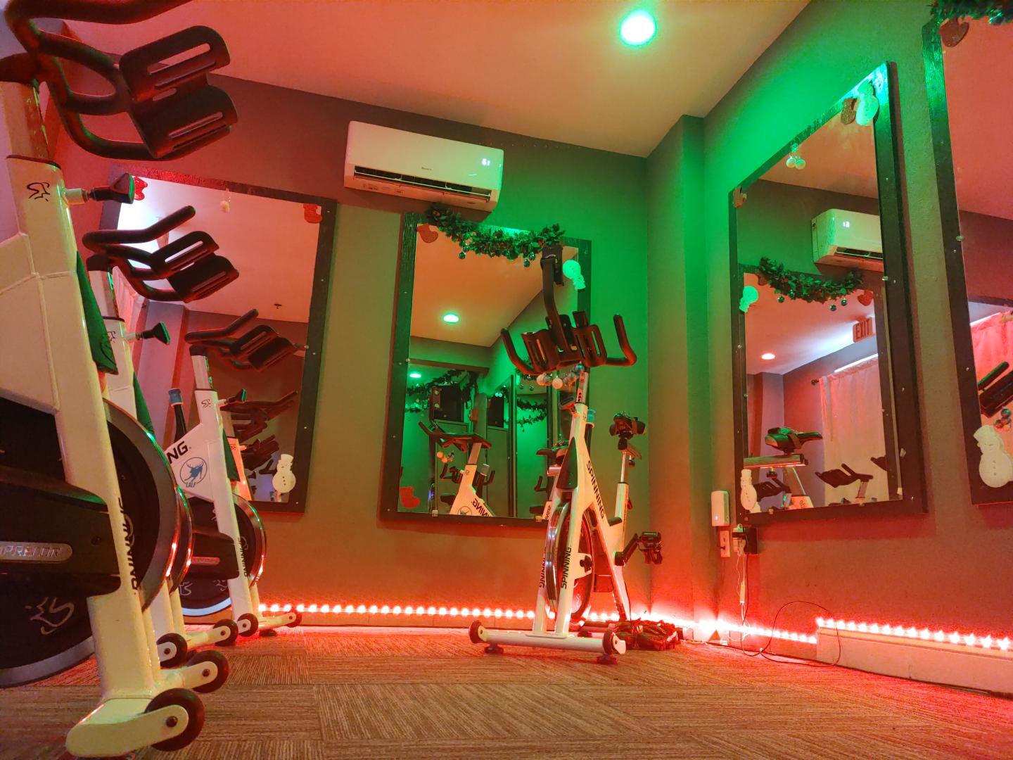 Fitness room with exercise bikes, mirrors, and green lighting.