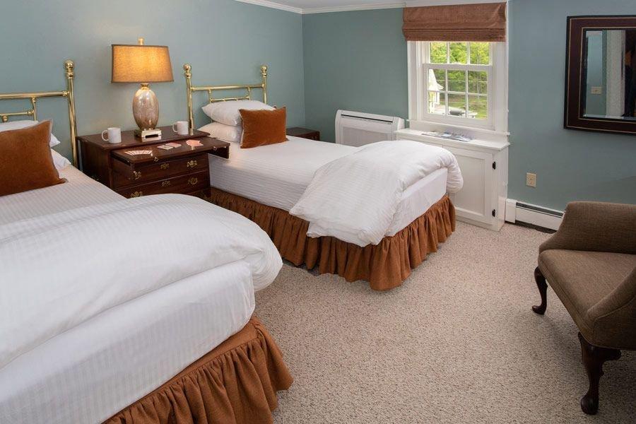 Two neatly made twin beds in a cozy bedroom with a window and chair.