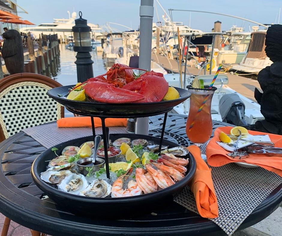 Seafood platter with lobster, shrimp, and oysters on a dockside table.