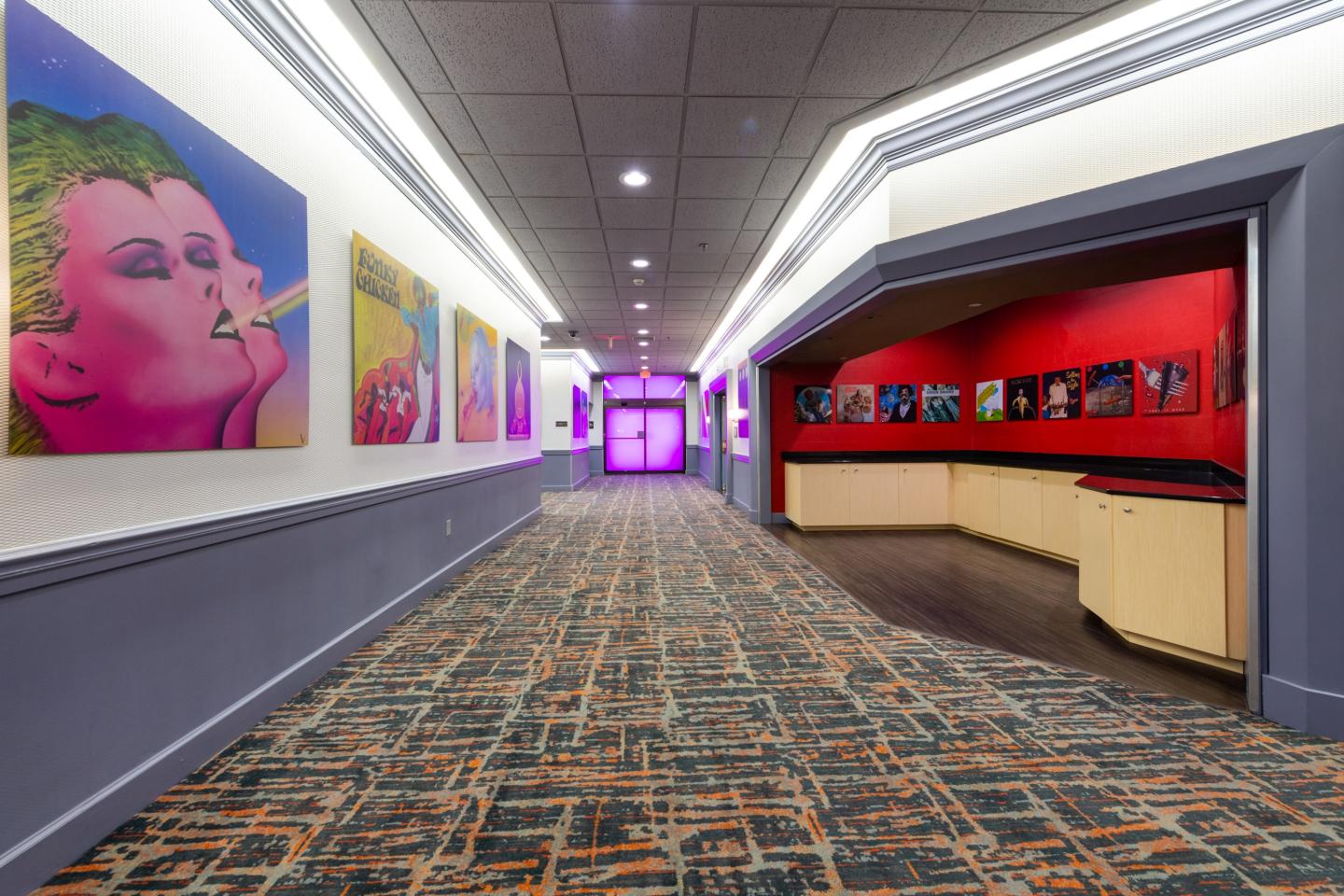 Hallway with colorful art on walls and patterned carpet.
