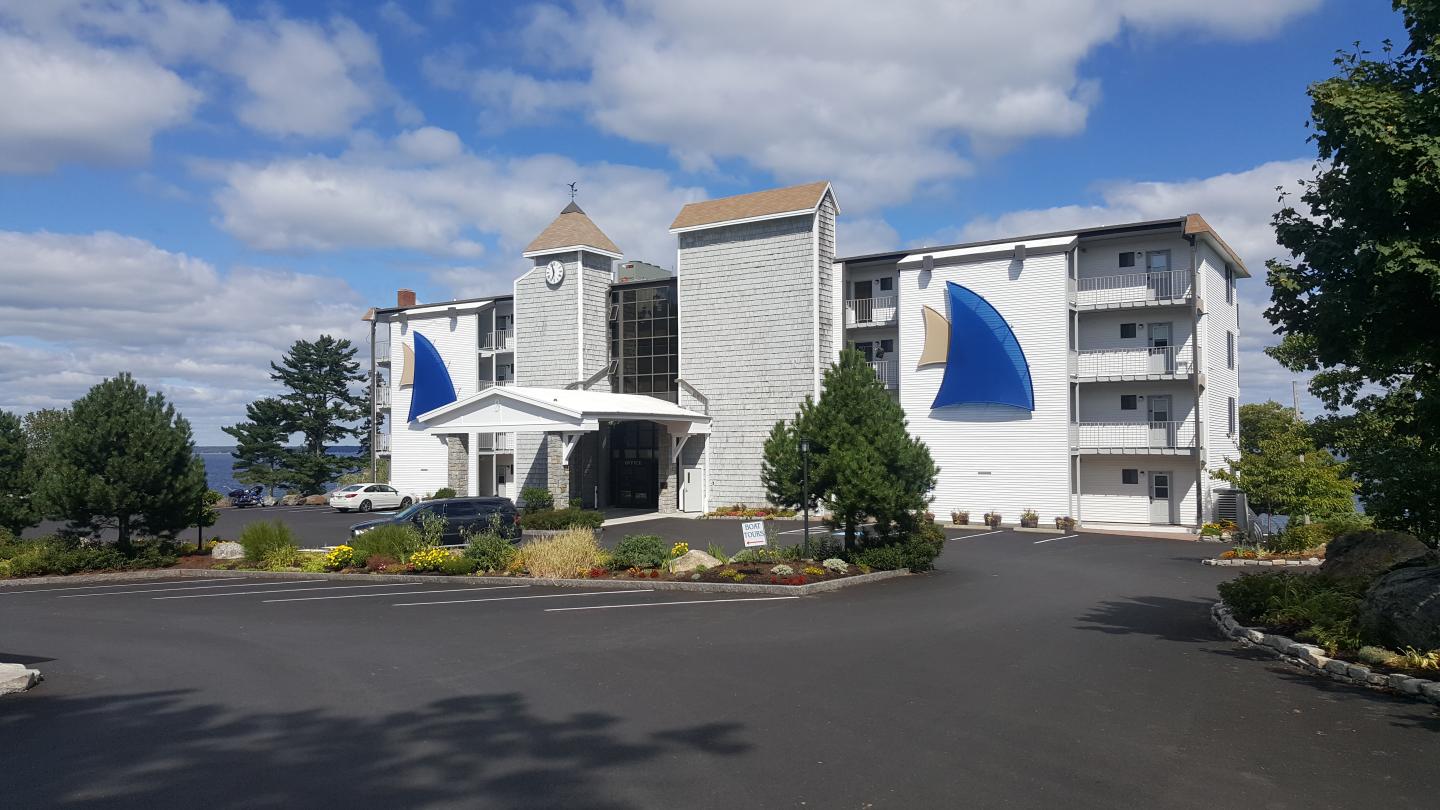 Modern hotel with white facade, blue sail designs, surrounded by trees and bright sky.