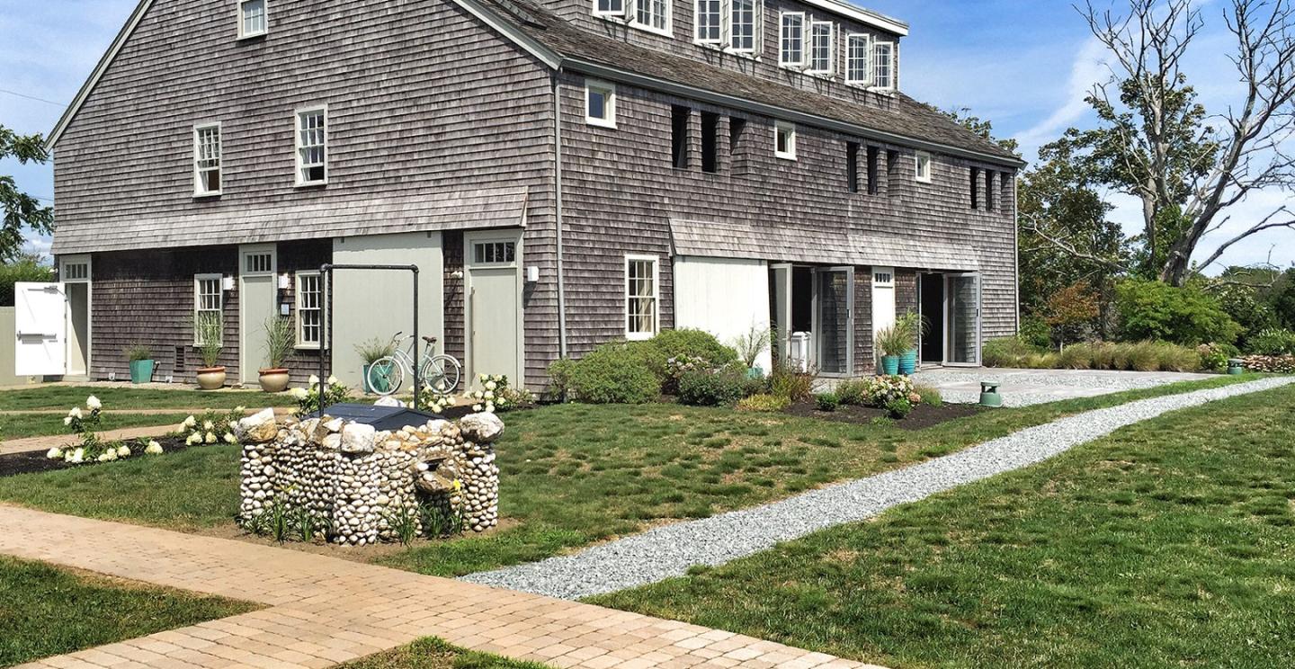 Grey shingled house with large windows, grassy yard, and stone garden feature.
