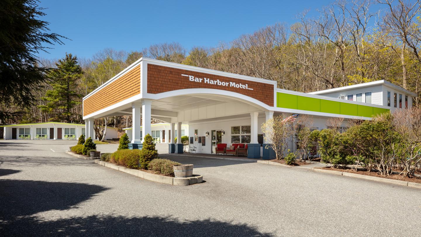 Retro-style motel entrance with a covered driveway, surrounded by trees.