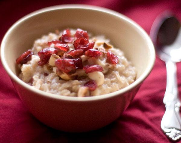Bowl of oatmeal topped with cranberries and nuts on a red cloth.