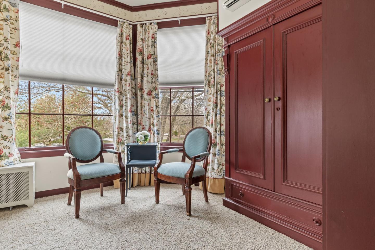 Two blue chairs near a window, with floral curtains and a wooden cabinet.