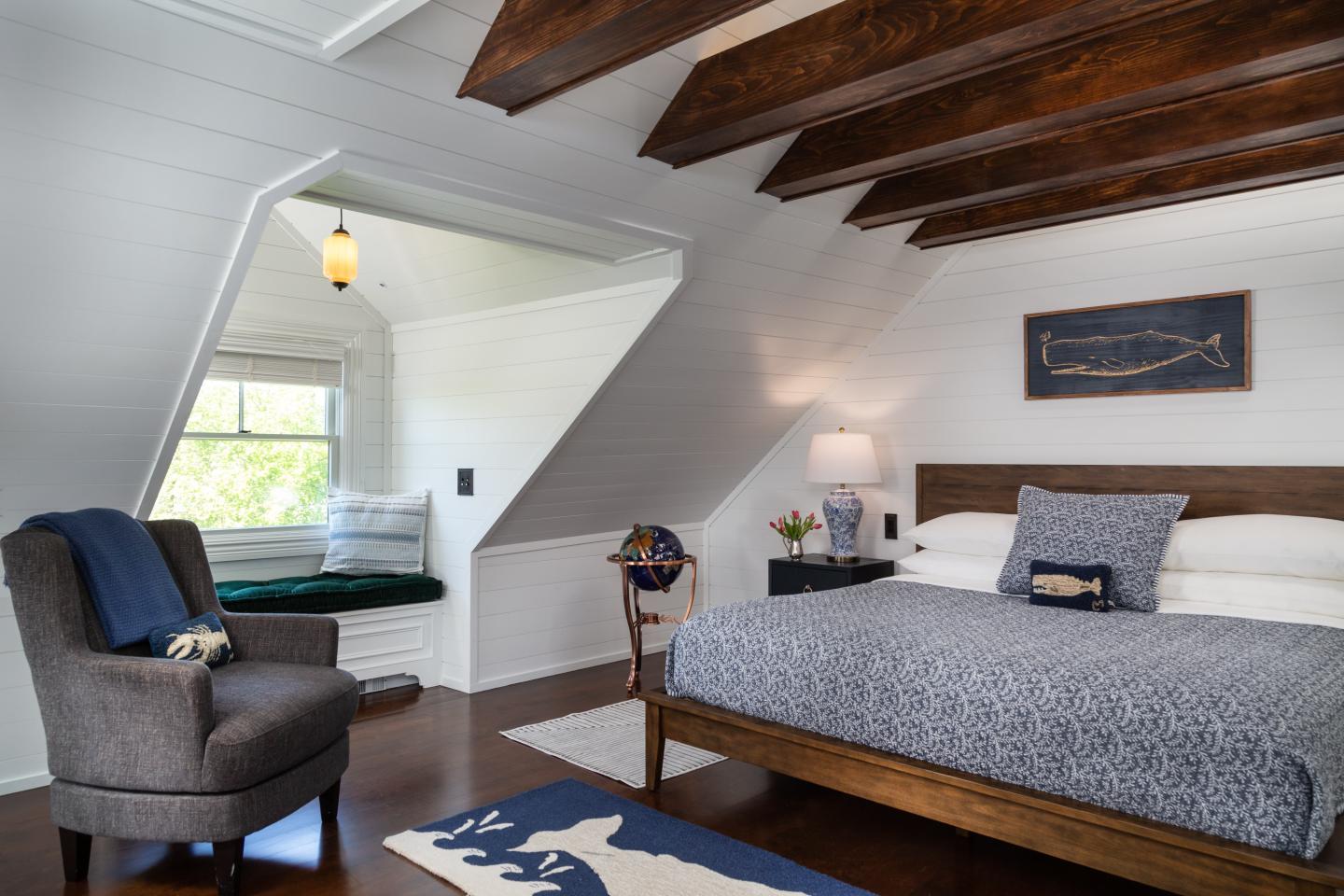 Cozy attic bedroom with a King bed, armchair, and window nook under wooden beams.