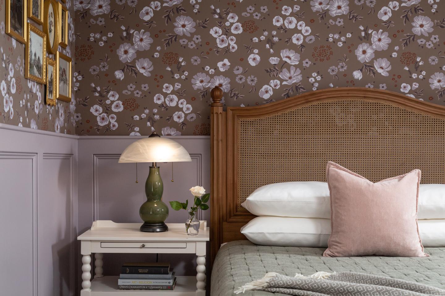 Bedside table with lamp, floral wallpaper, and framed pictures above.