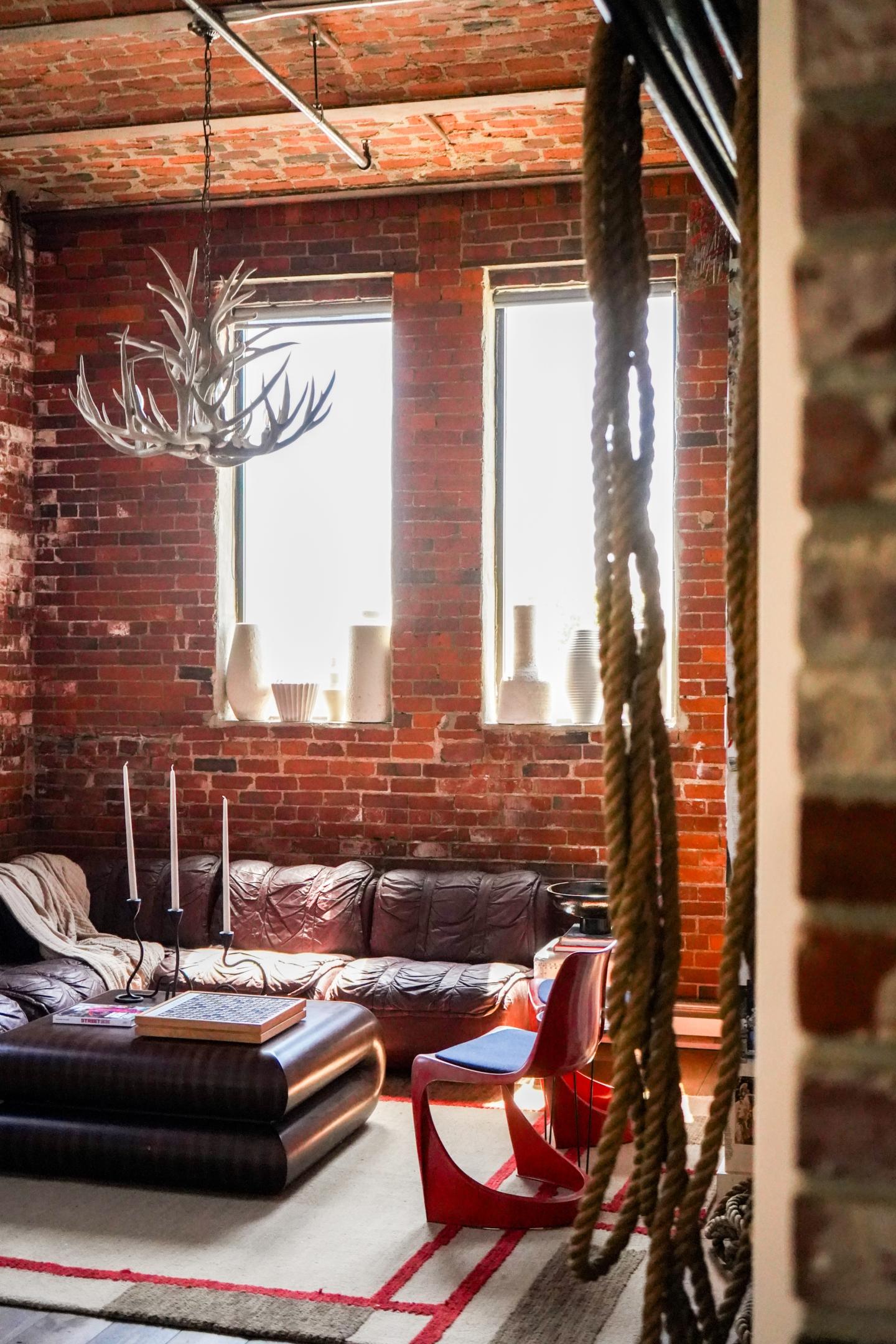 Loft living room with brick walls, leather sofa, and antler chandelier.
