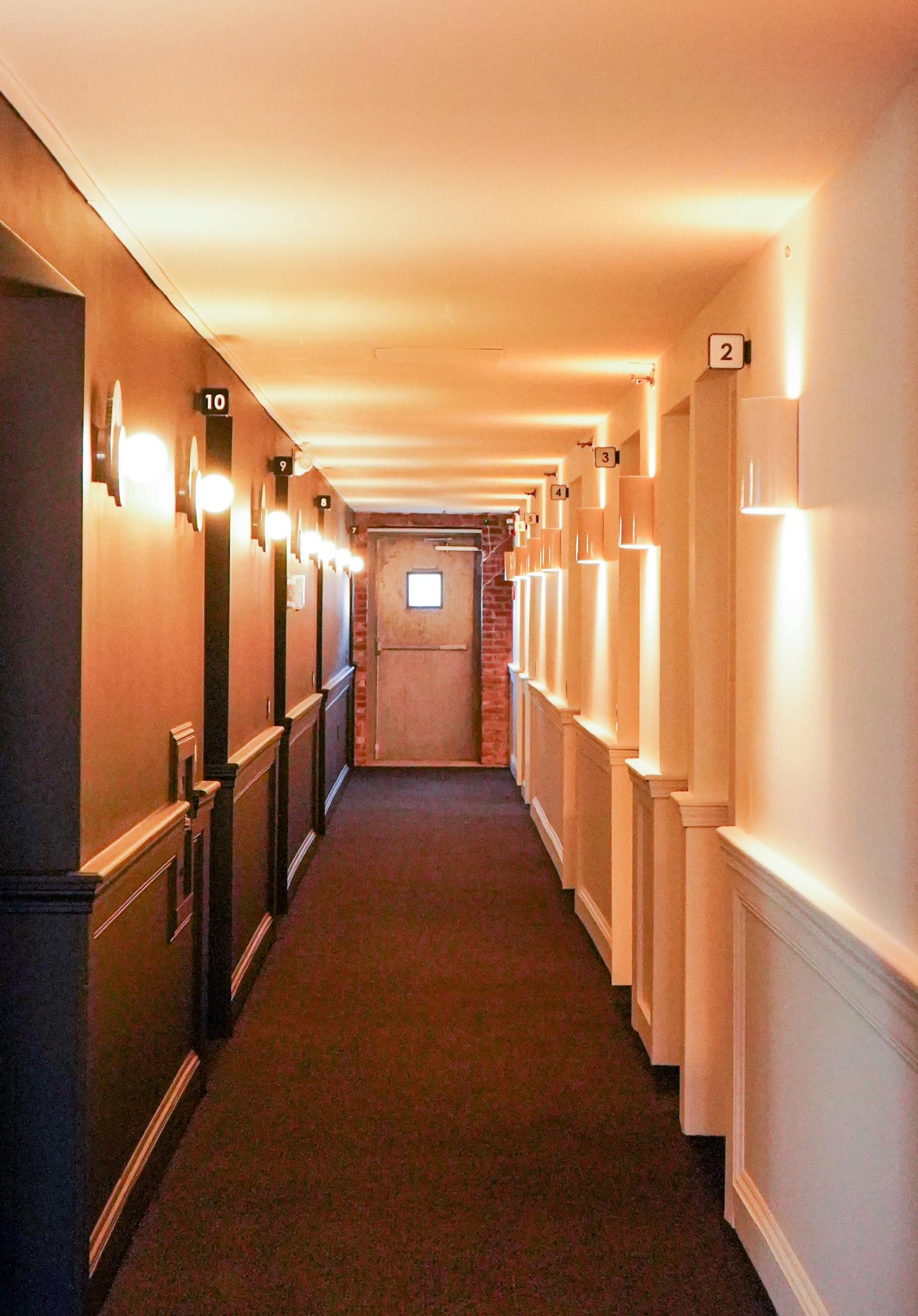 Narrow hallway with warm lighting and a closed wooden door at the end.
