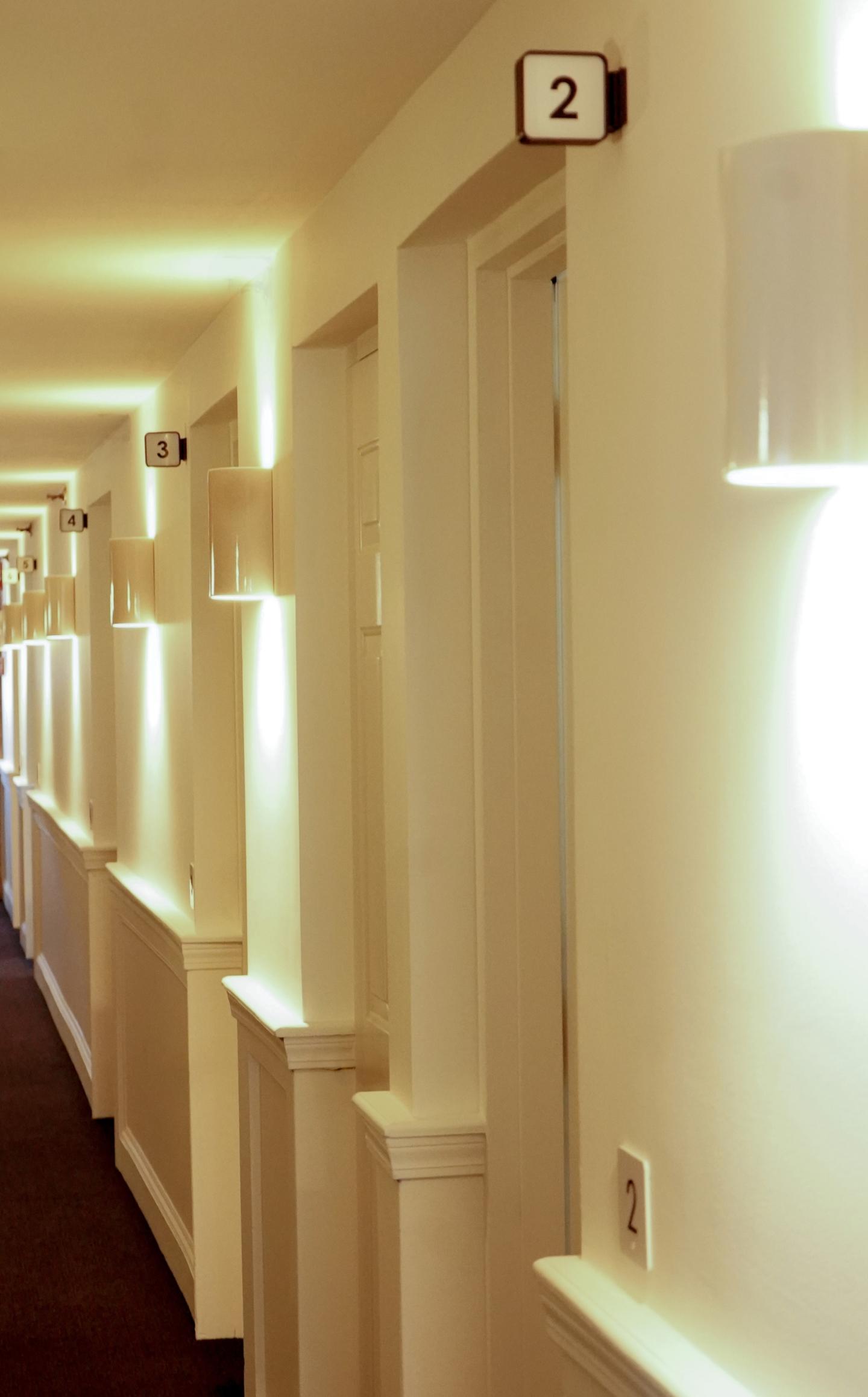 Brightly lit hotel hallway with numbered doors.
