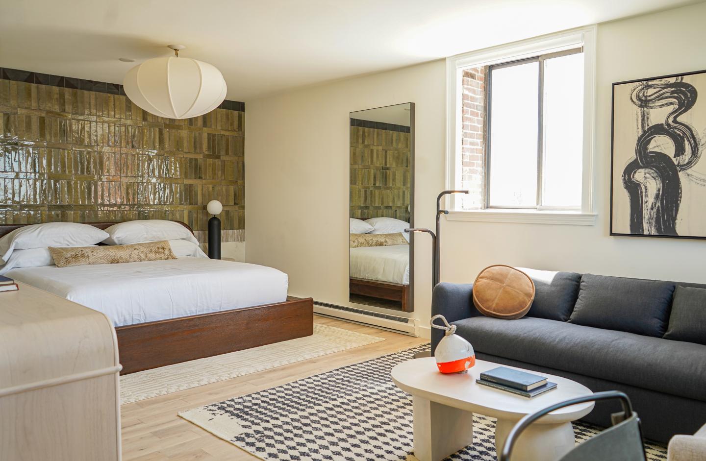 Stylish bedroom with bed, couch, mirror, and abstract art on wall.