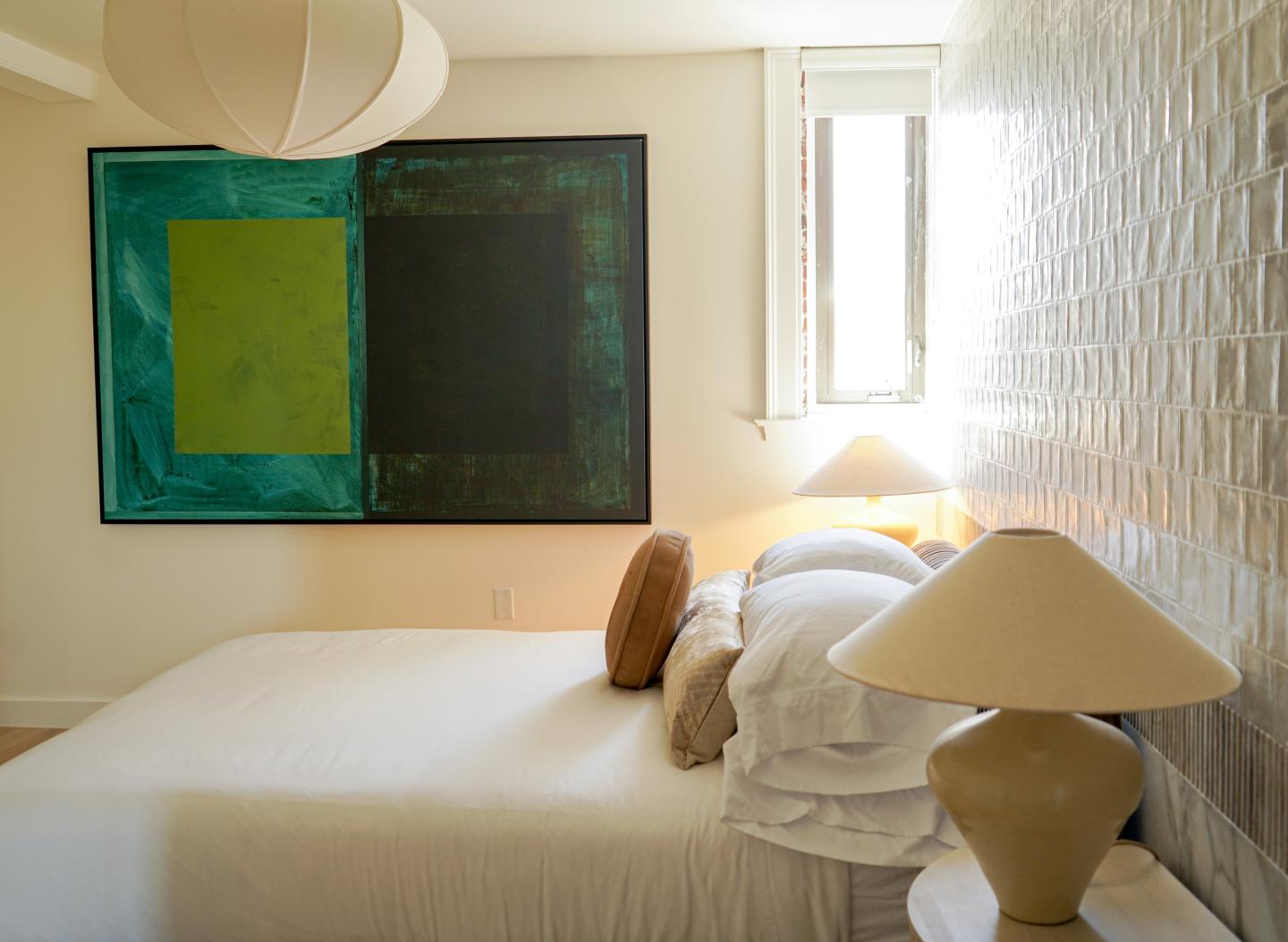 Minimalist bedroom with a bed, lamp, and abstract wall art.