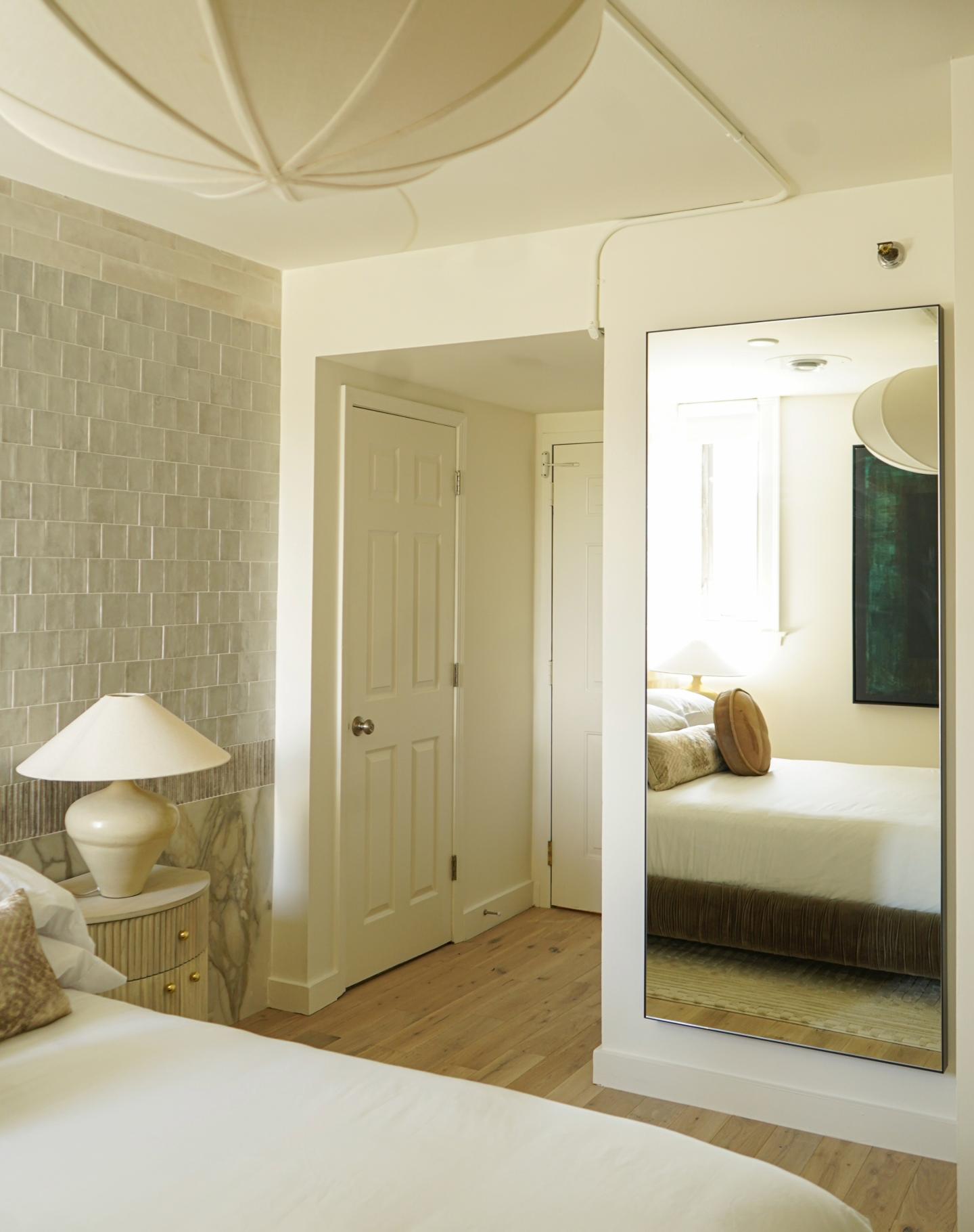 Cozy bedroom with beige walls, lamp, and large mirror.