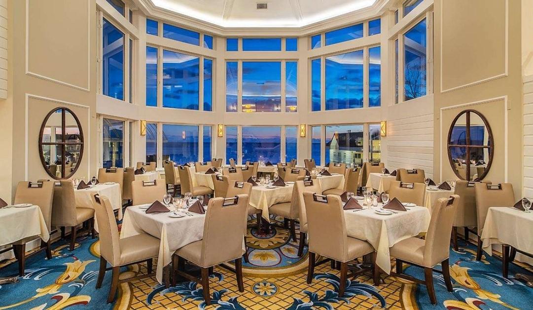 Elegant dining room with ocean view, beige chairs, and white tablecloths.