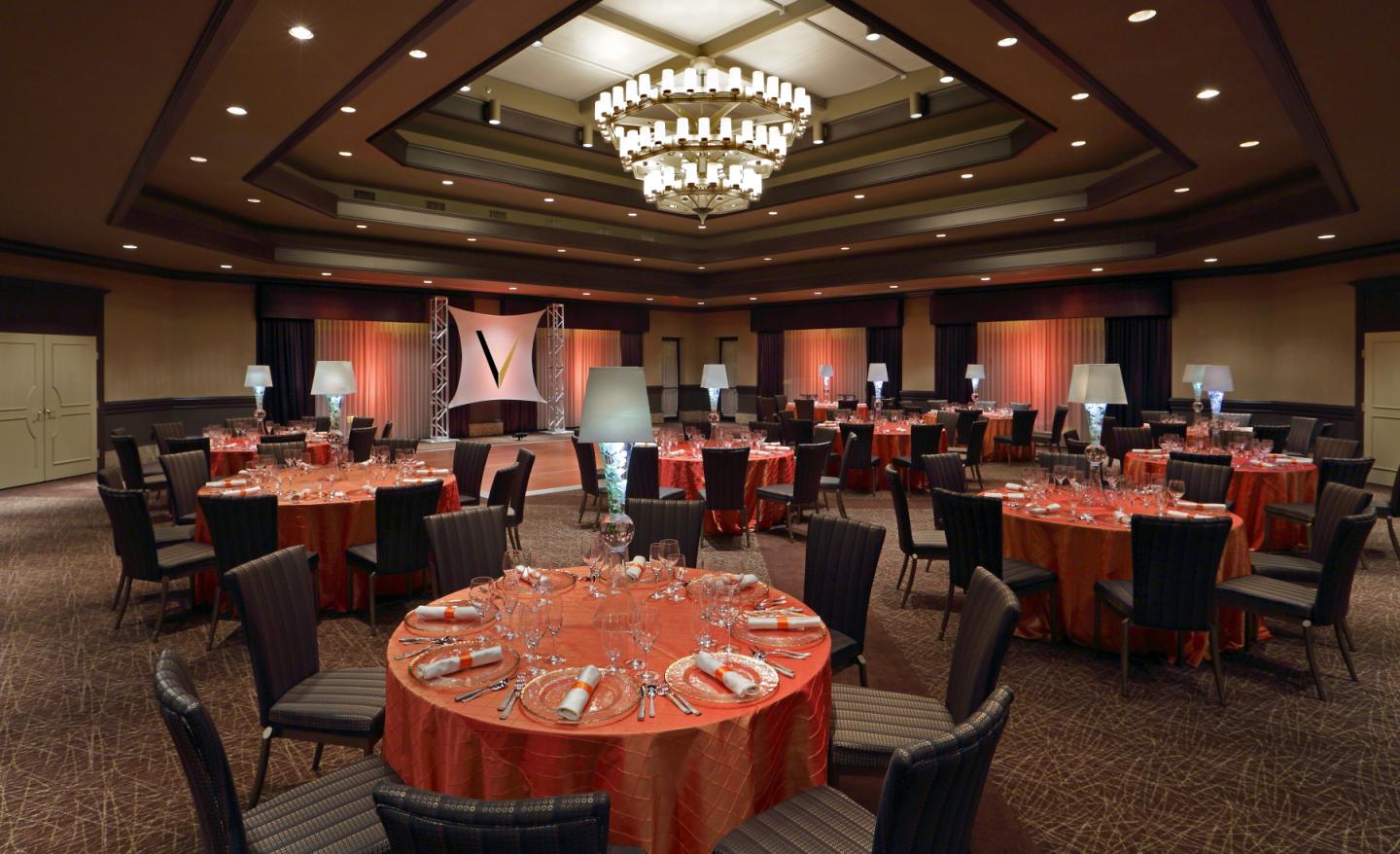 Elegant banquet room with round tables, red tablecloths, and chandeliers.