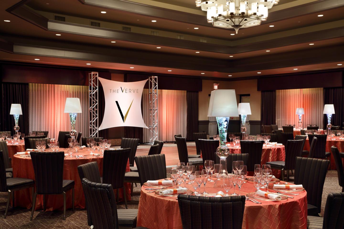 Elegant banquet hall with round tables set for dinner, warm lighting, large chandelier.